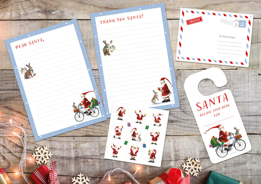 Two sheets of letter paper with a light blue boarder. The letter paper with red text at the top that reads "Dear Santa," features illustrations of a hare wearing a knitted scarf with a sprig of holly and a robin, and Santa riding a bicycle laden with presents and a hare in a knitted scarf sitting in the basket. The letter paper with red text at the top reads "thank you Santa!" features illustrations of a hare wearing a knitted scarf with a sprig of holly and a robin